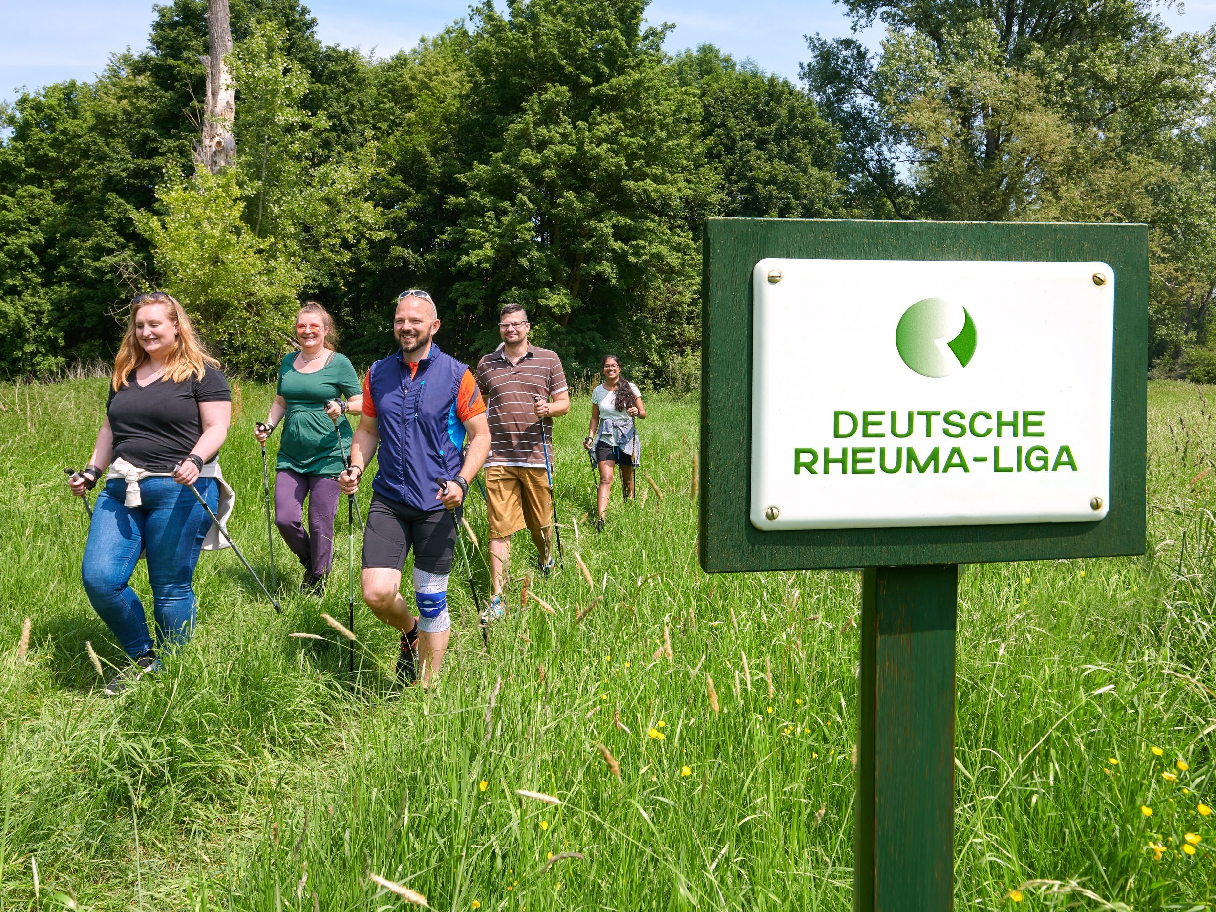 Gruppe von Menschen beim Nordic Walken, im Vordergrund Schild mit der Aufschrift "Deutsche Rheumaliga Bundesverband"
