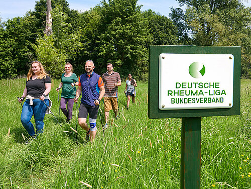Gruppe von Menschen beim Nordic Walken, im Vordergrund Schild vom Deutschen Rheumaliga Bundesverband